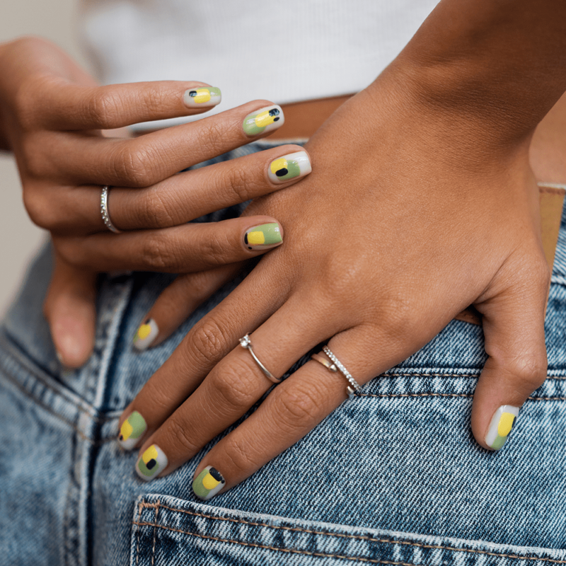 une femme montre sa manucure tricolore : vert jaune et une pointe de noir